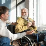 an old man sitting on a wheelchair while talking to a man
